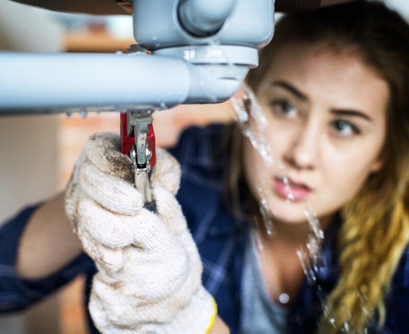 Woman fixing a leaking pipe under a sink