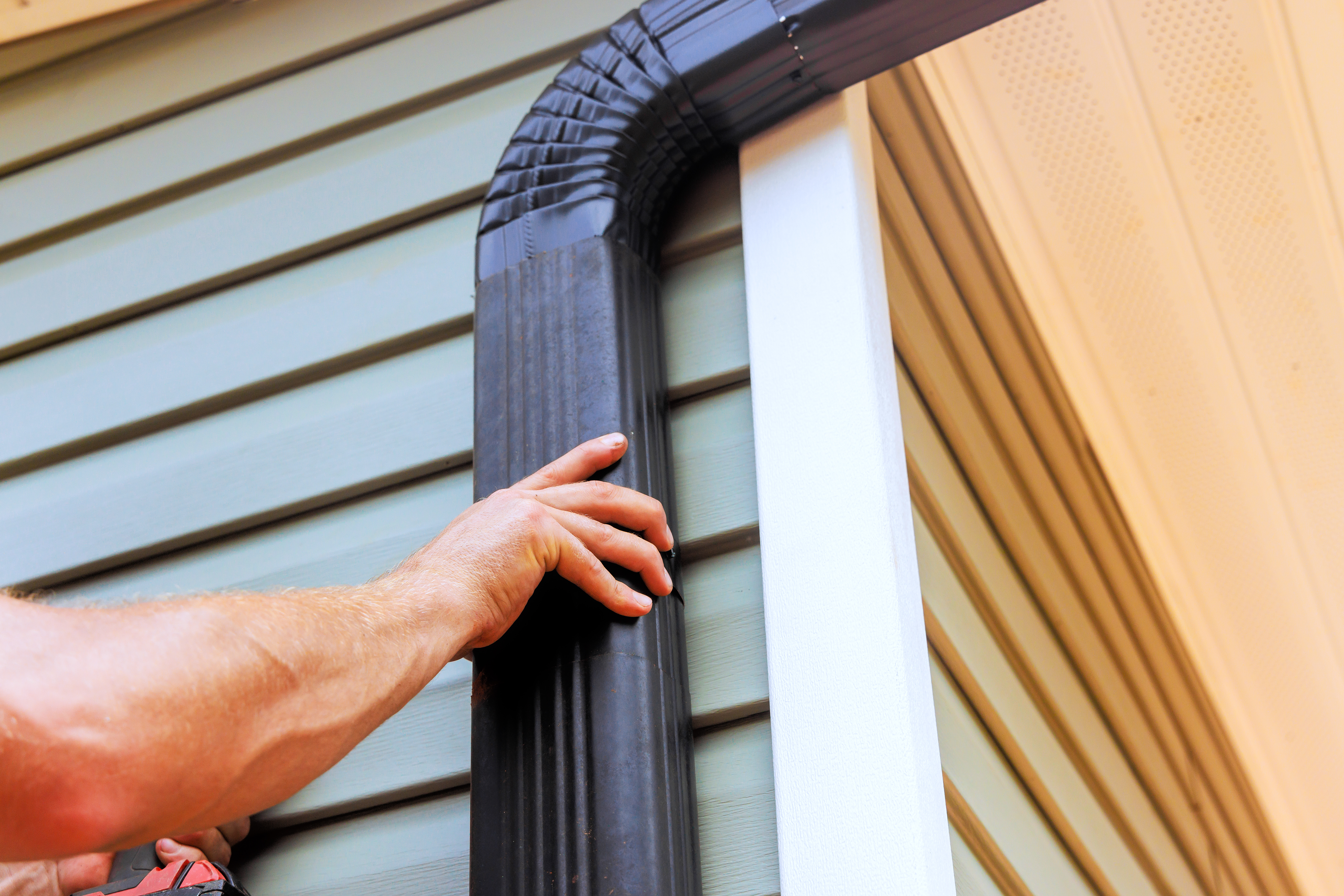 Worker installing rain gutter downspout on residential home